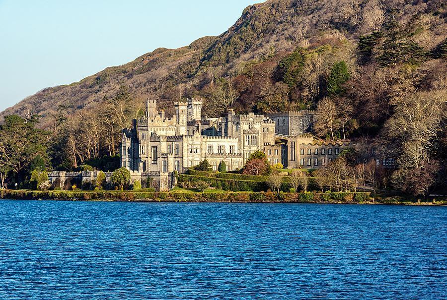 Historic castle surrounded by lush greenery and a serene lake, set against a mountainous backdrop, showcasing architectural beauty and natural landscapes.