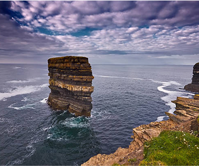 "Scenic view of a rocky sea stack rising from the ocean, surrounded by waves and under a cloudy sky, showcasing the natural beauty of the coastline."