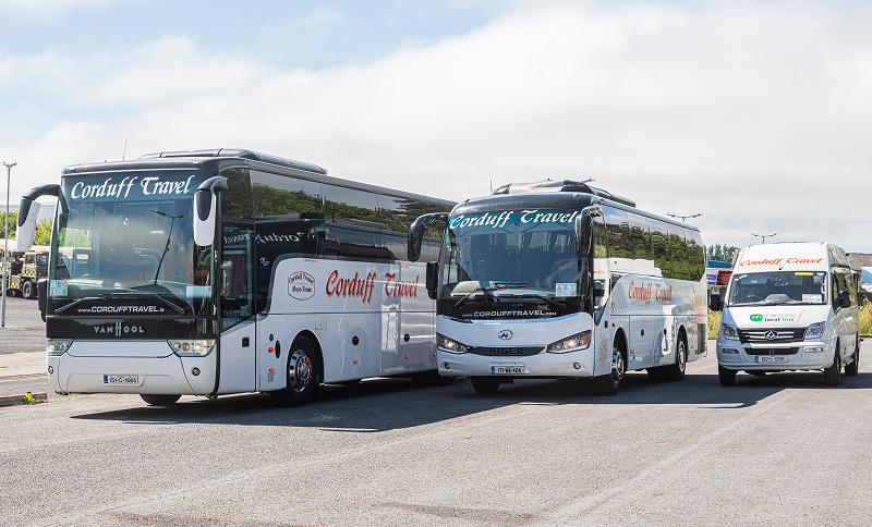 "Corduff Travel coaches parked at a terminal, featuring two large buses and a smaller van, all branded with the Corduff Travel logo. The image showcases the modern fleet in a sunny outdoor setting, highlighting transportation options for group travel and tours."