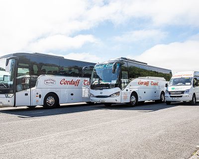 A fleet of Corduff Travel vehicles, including two large coaches and a smaller van, parked in a row on a sunny day.