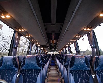 Interior view of a spacious, modern bus with blue patterned seats and overhead lighting, showcasing the arrangement of rows and aisle.