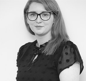 Alt text: Woman with long hair wearing glasses and a black blouse with decorative dots, posing against a plain background.