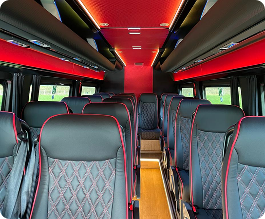 Interior of a Corduff Travel luxury coach showing black quilted leather seats with red accents, ambient lighting, and a clean, comfortable layout designed for modern group travel across Irela