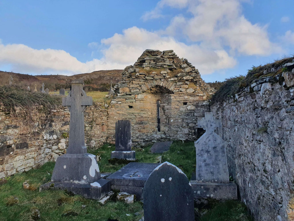 "Historic graveyard with stone crosses and ruins of an old building under a blue sky with clouds"