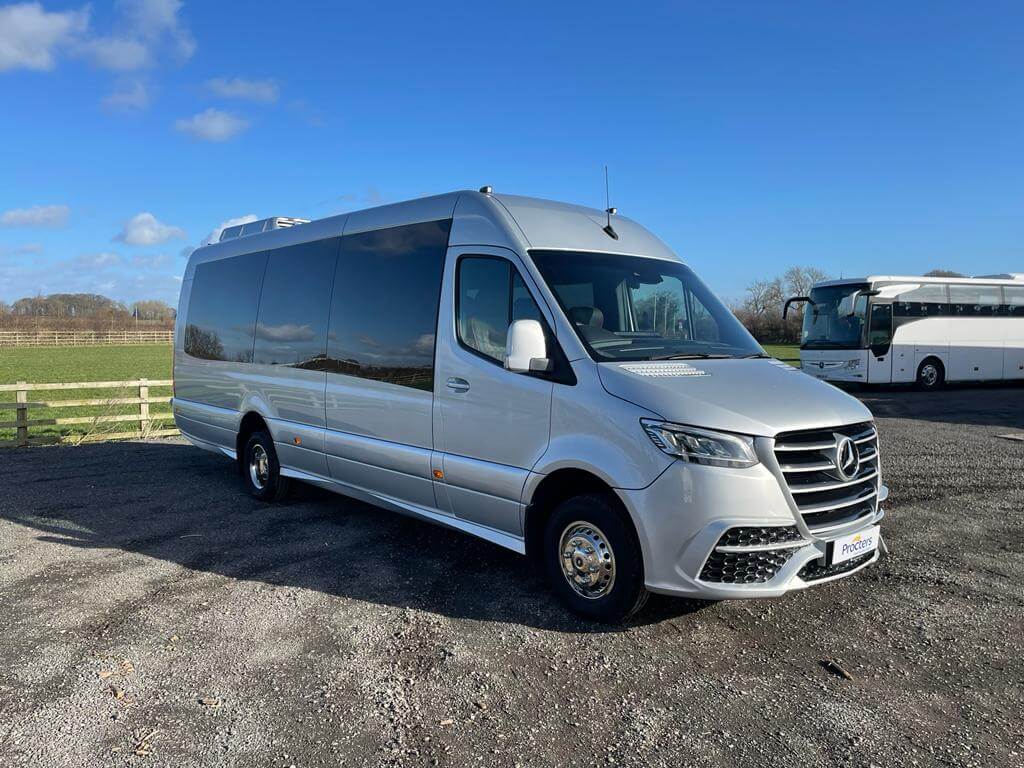 Silver Mercedes-Benz Sprinter van parked in a gravel lot with a scenic countryside background, showcasing its spacious design and modern features, ideal for group transportation or shuttle services.