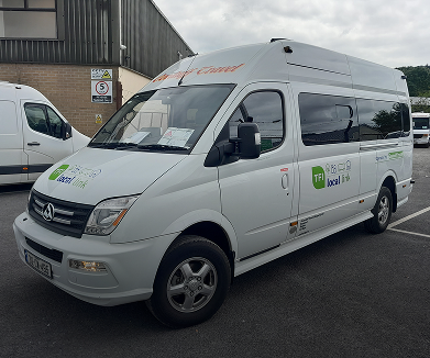 Alt text: White passenger van with branding for local transport services, parked in a lot with other vehicles in the background.